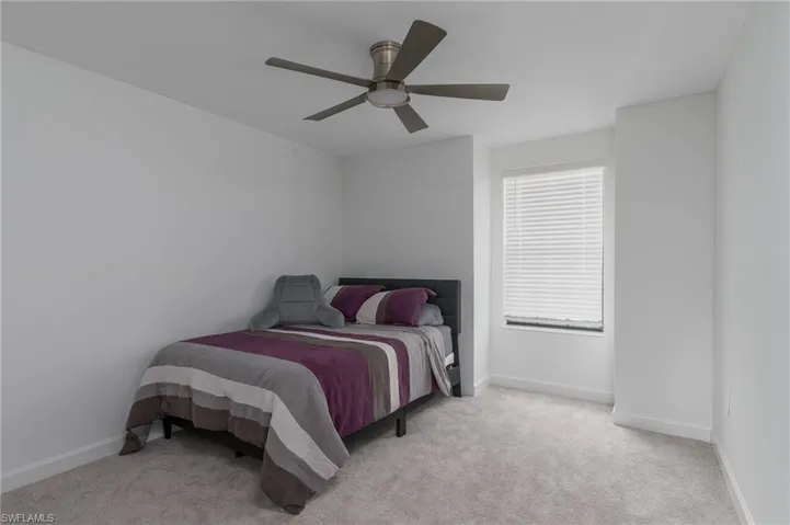 Bedroom featuring light gray carpeting, neutral white walls, a single window with horizontal blinds, and a ceiling fan with brushed nickel finishes