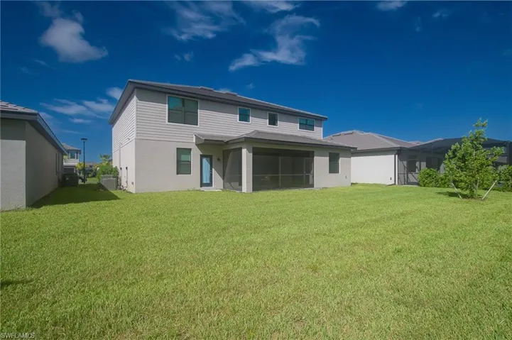 Expansive green lawn surrounds the rear exterior, featuring a screened patio