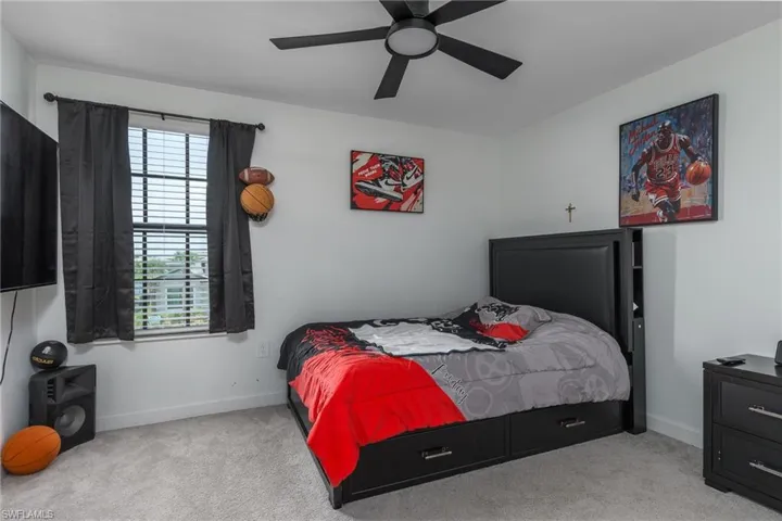 Carpeted room featuring a ceiling fan with integrated lighting, a window with horizontal blinds, and a built-in storage bed frame