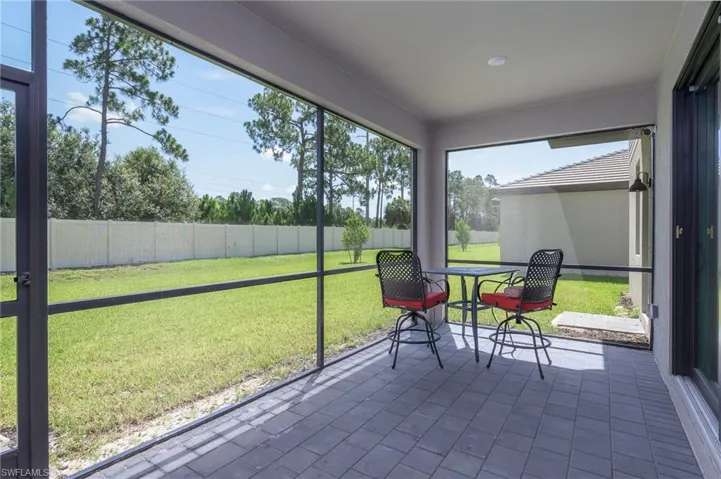 Screened lanai featuring gray paver flooring, exterior wall-mounted lighting, and a white privacy fence enclosing a manicured lawn