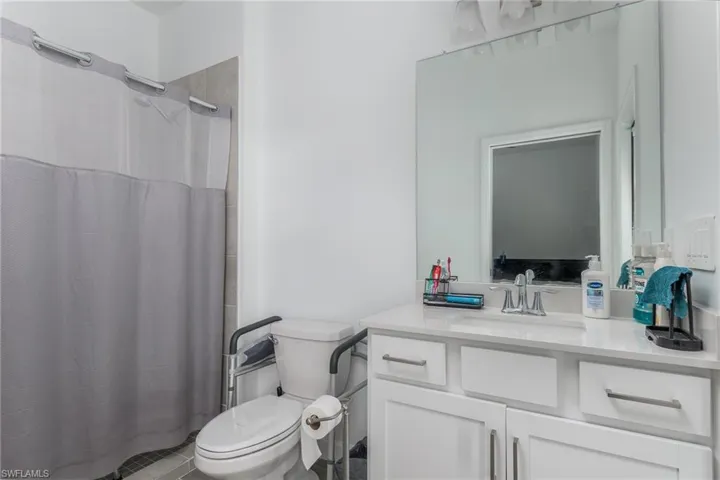 Bathroom featuring a white vanity with a light-toned countertop, a large wall-mounted mirror, and a shower with tiled walls