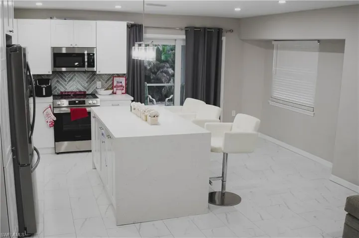 Kitchen featuring a kitchen island, appliances with stainless steel finishes, white cabinets, decorative backsplash, and hanging light fixtures