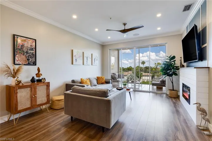 Living room with ornamental molding, wood finished floors, a glass covered fireplace, recessed lighting, and ceiling fan