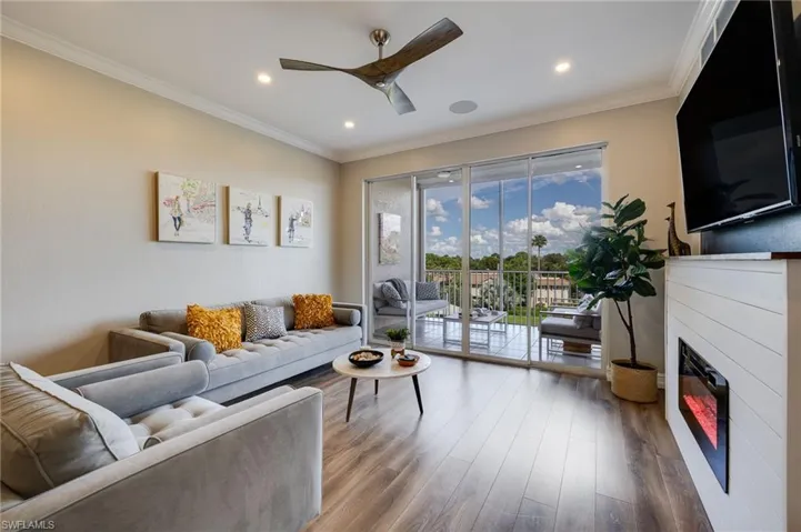 Living room featuring a glass covered fireplace, ornamental molding, wood finished floors, a ceiling fan, and recessed lighting