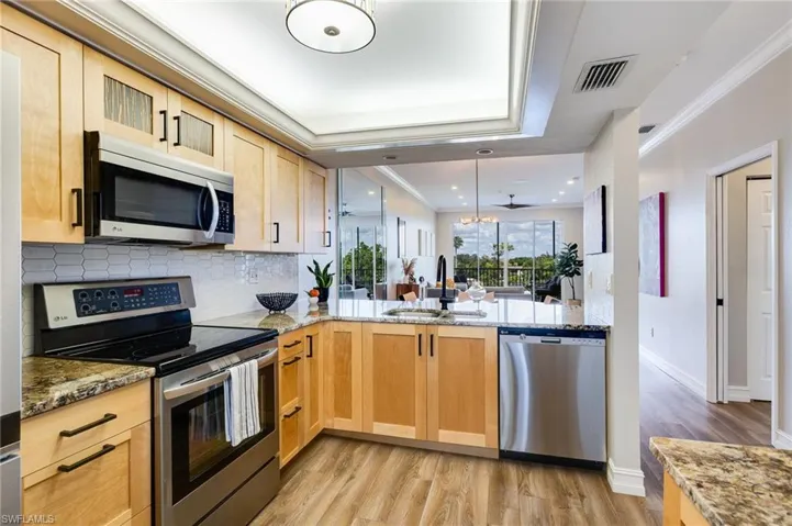 Kitchen with appliances with stainless steel finishes, ornamental molding, light stone countertops, decorative light fixtures, and light wood finished floors