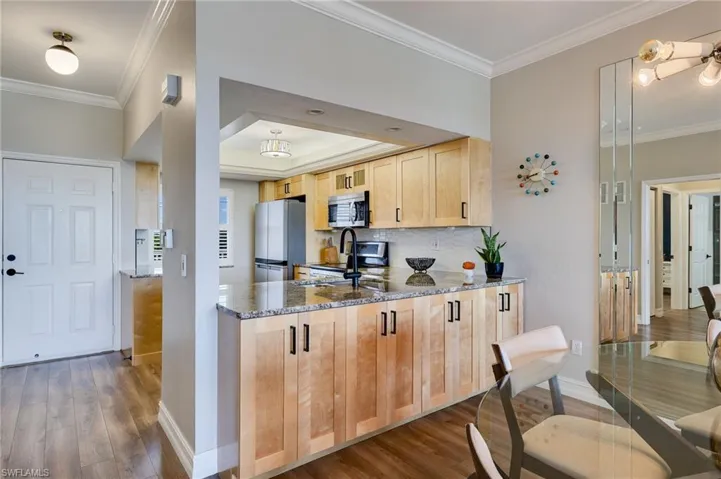 Kitchen with dark stone countertops, ornamental molding, light wood-type flooring, light brown cabinetry, and appliances with stainless steel finishes