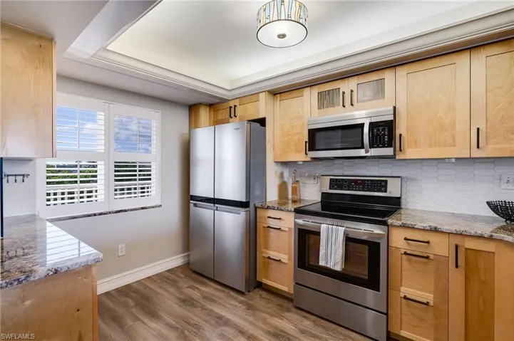 Kitchen with dark stone countertops, stainless steel appliances, backsplash, dark wood finished floors, and light brown cabinetry