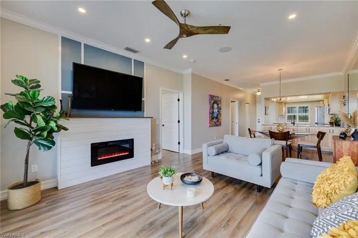 Living room with ornamental molding, wood finished floors, a glass covered fireplace, a ceiling fan, and recessed lighting