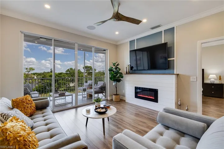 Living room with crown molding, wood finished floors, a glass covered fireplace, recessed lighting, and ceiling fan