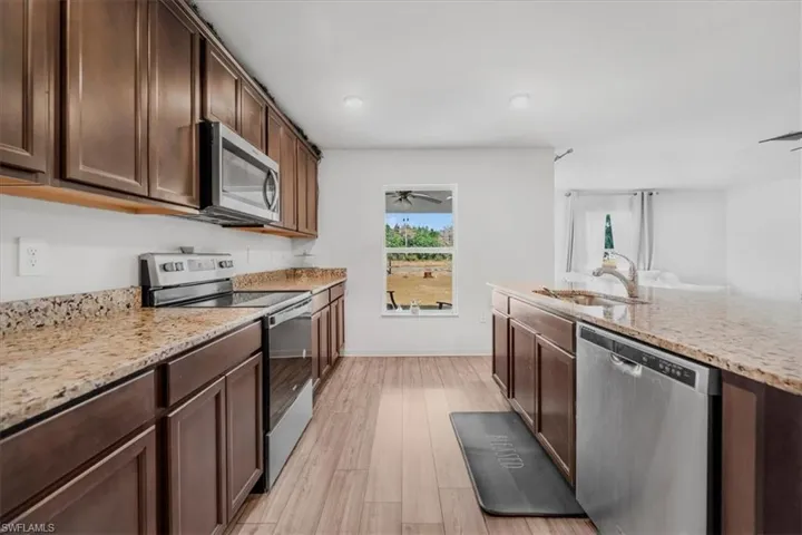 Kitchen featuring stainless steel appliances, light stone counters, light wood-type flooring, dark wood finish cabinetry, and open floor plan
