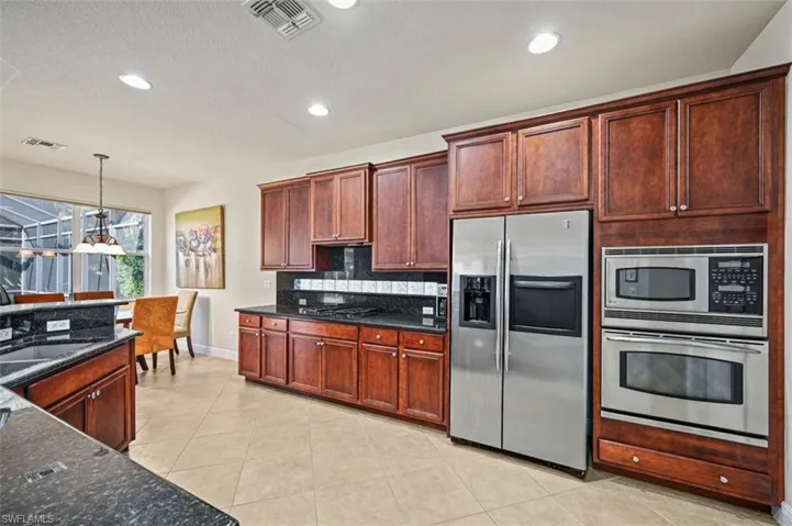 Kitchen with stainless steel appliances, decorative light fixtures, recessed lighting, light tile patterned floors, and dark stone counters