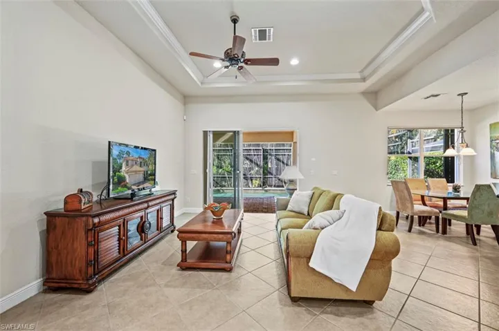 Living area with ceiling fan, healthy amount of natural light, a raised ceiling, light tile patterned floors, and recessed lighting