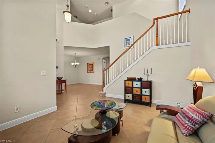 Living area featuring light tile patterned flooring, a towering ceiling, a chandelier, and stairs