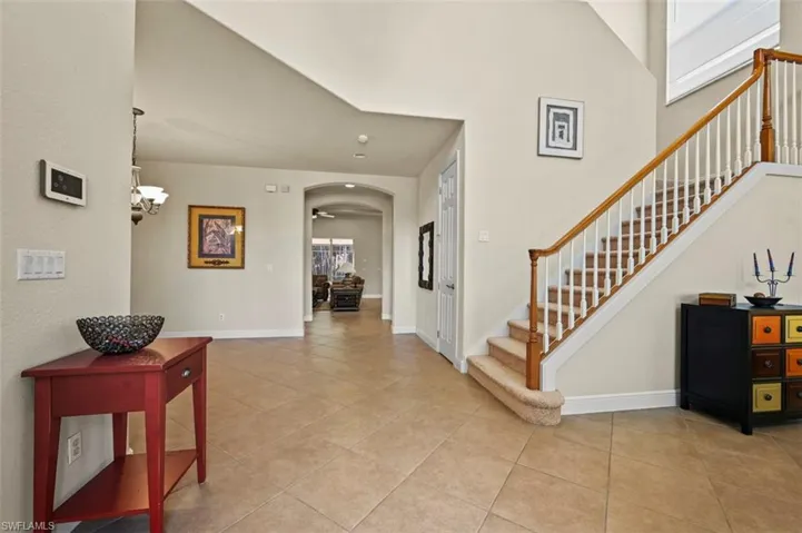 Foyer entrance with arched walkways, light tile patterned floors, stairway, a ceiling fan, and a towering ceiling