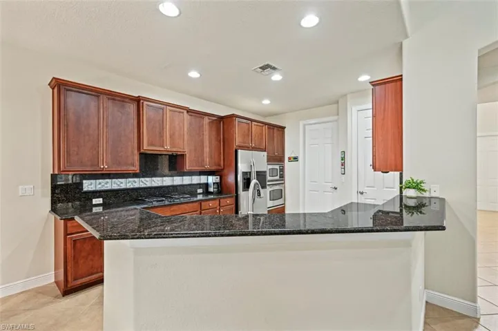 Kitchen featuring light tile patterned floors, dark stone countertops, backsplash, appliances with stainless steel finishes, and recessed lighting