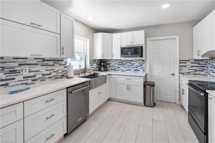 Kitchen with white cabinets, stainless steel appliances, light stone counters, recessed lighting, and decorative backsplash
