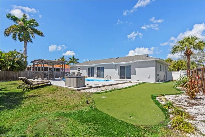Back of property featuring a patio, a fenced backyard, a pergola, stucco siding, and a putting green