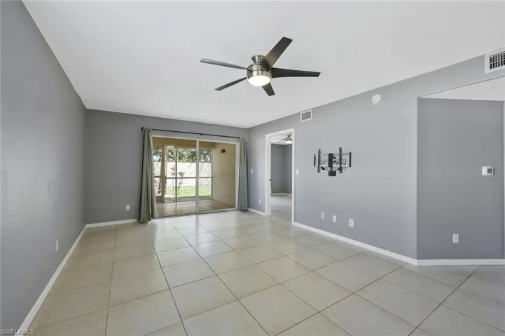 Empty room with visible vents, light tile patterned floors, ceiling fan, and baseboards