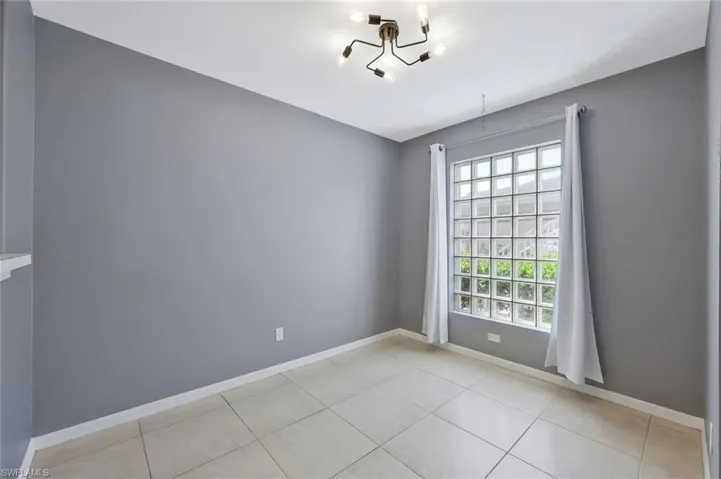 Unfurnished room with light tile patterned floors, baseboards, and an inviting chandelier