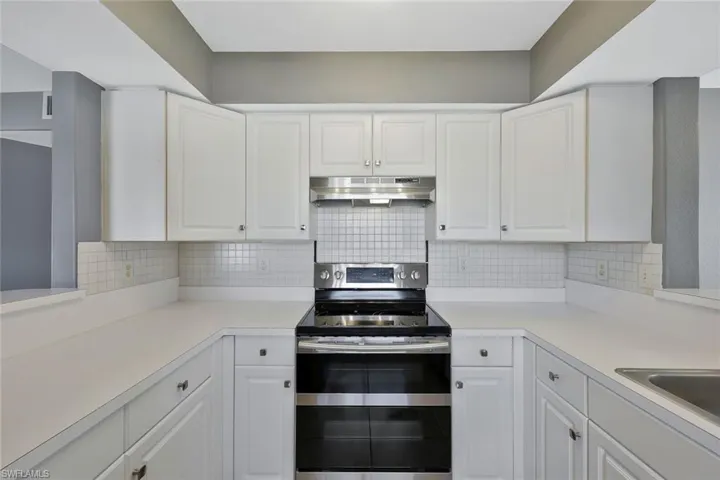 Kitchen with under cabinet range hood, range with two ovens, and white cabinets