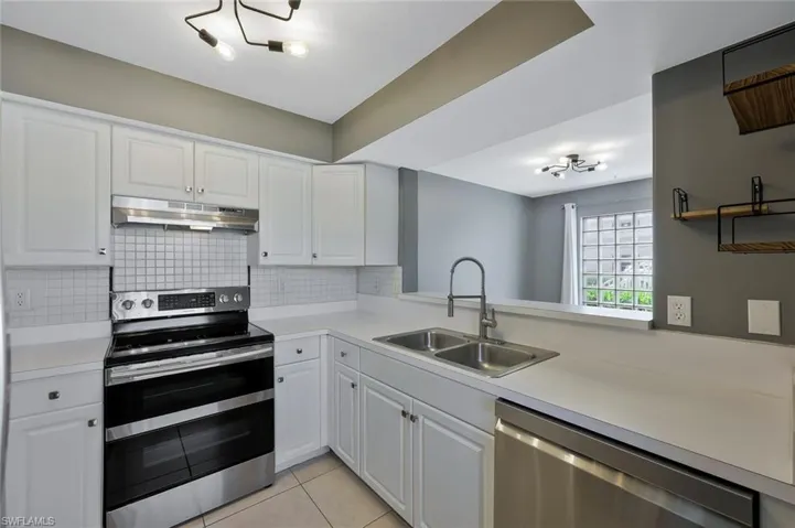 Kitchen with stainless steel appliances, under cabinet range hood, light countertops, and a sink
