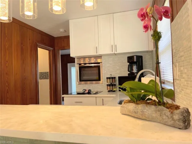 Kitchen featuring white cabinetry, oven, pendant lighting, tasteful backsplash, and light stone counters