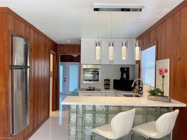 Kitchen with wooden walls, decorative light fixtures, light tile patterned floors, a peninsula, and black appliances