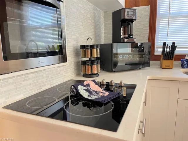 Kitchen featuring black appliances, light stone counters, backsplash, and white cabinetry