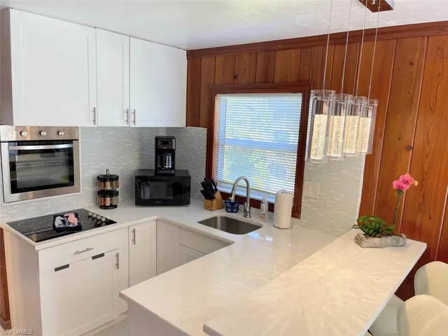 Kitchen with black appliances, white cabinetry, backsplash, a peninsula, and light stone countertops