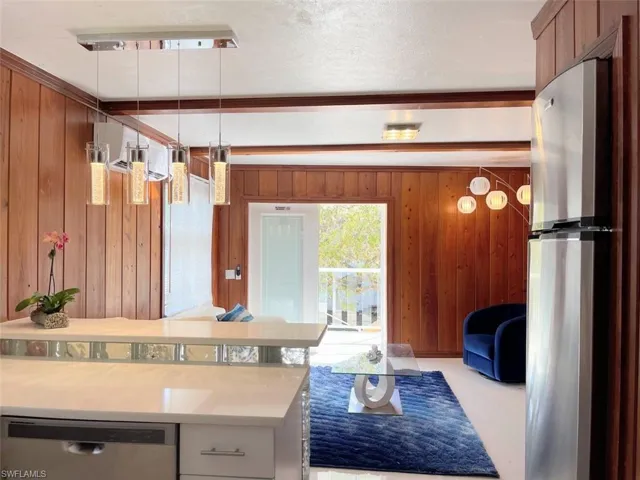 Kitchen featuring hanging light fixtures, appliances with stainless steel finishes, wooden walls, beam ceiling, and light stone counters