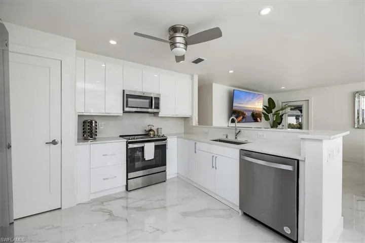 Kitchen with appliances with stainless steel finishes, white cabinetry, light marble finish flooring, a peninsula, and recessed lighting