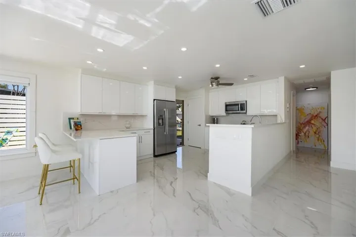 Kitchen with a peninsula, white cabinetry, a kitchen breakfast bar, stainless steel appliances, and recessed lighting