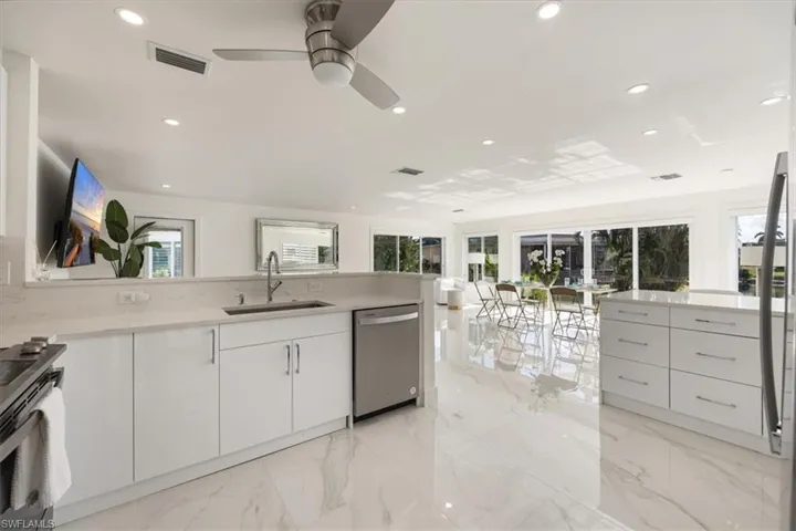 Kitchen featuring a peninsula, stainless steel appliances, light stone counters, light marble finish floors, and healthy amount of natural light