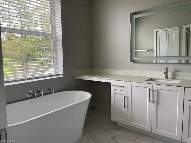 Full bathroom with vanity, a soaking tub, and light marble finish floors