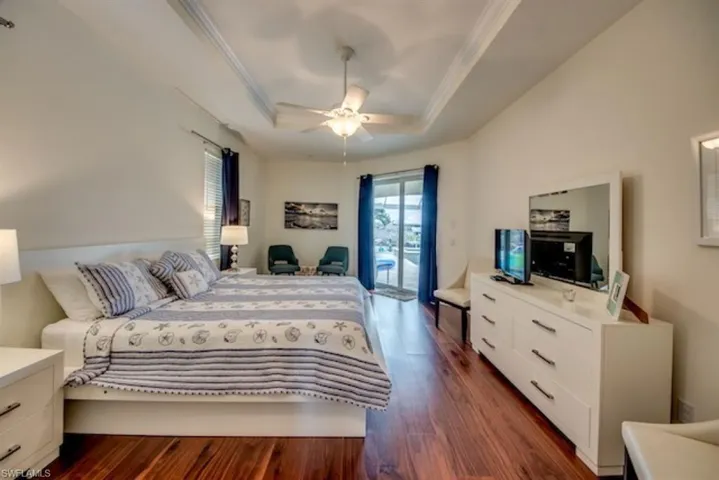 Bedroom featuring dark hardwood / wood-style floors, ceiling fan, a tray ceiling, and access to outside
