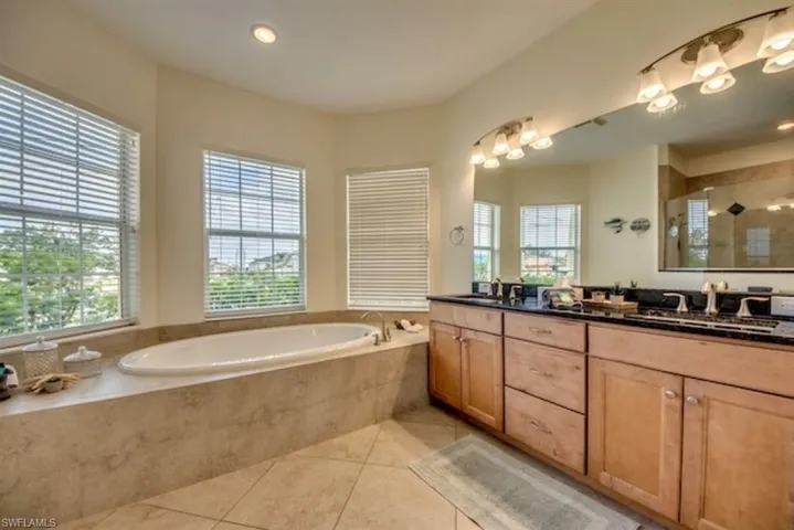 Bathroom featuring tile flooring, tiled bath, and double sink vanity