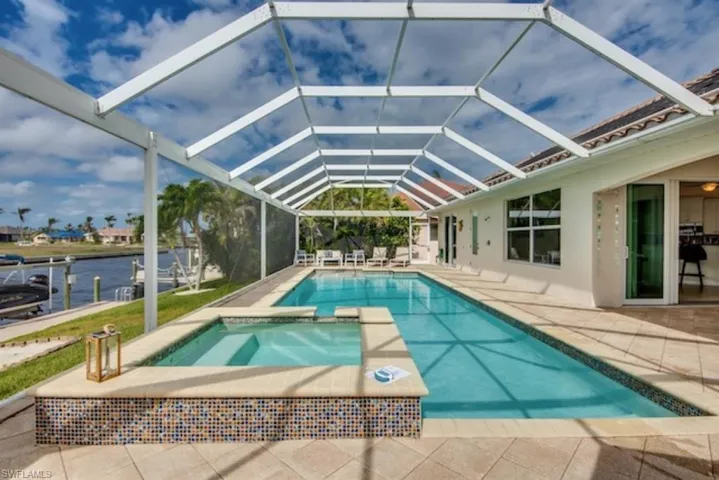 View of swimming pool featuring a patio, glass enclosure, an in ground hot tub, and a water view