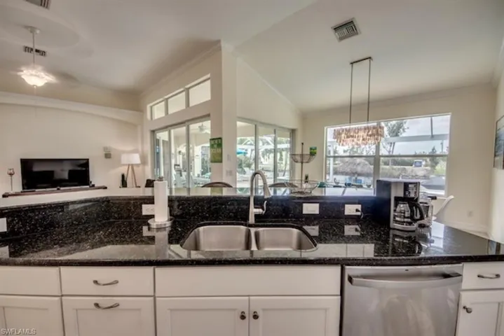 Kitchen with sink, white cabinets, dark stone countertops, and stainless steel dishwasher