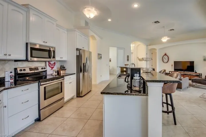 Kitchen with a center island with sink, tasteful backsplash, white cabinetry, appliances with stainless steel finishes, and light tile floors