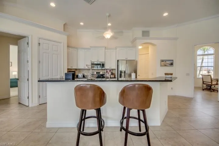 Kitchen with stainless steel appliances, white cabinets, light tile floors, and a kitchen island with sink