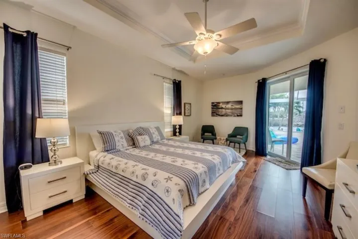 Bedroom with ceiling fan, access to exterior, a tray ceiling, and hardwood / wood-style floors