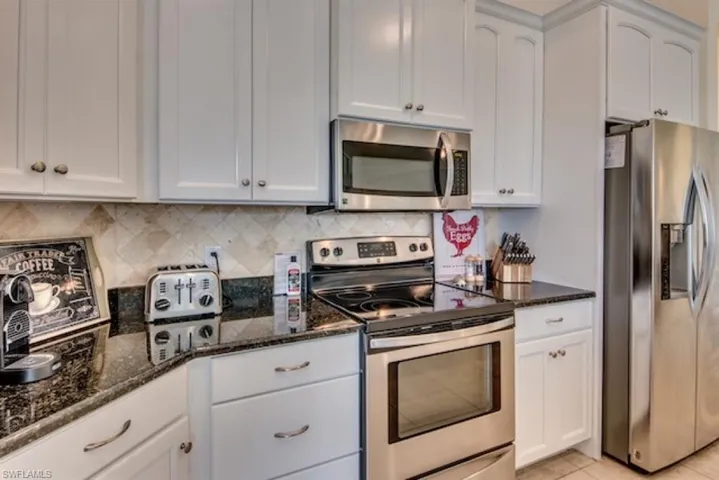 Kitchen featuring white cabinetry, dark stone counters, light tile flooring, and stainless steel appliances
