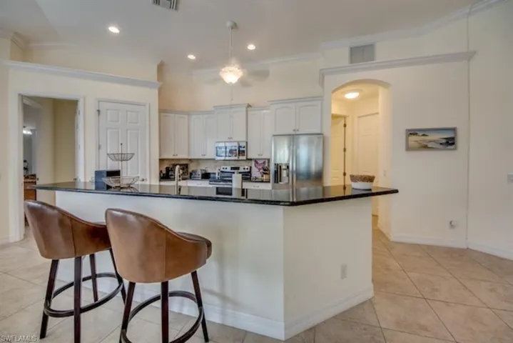 Kitchen featuring backsplash, light tile floors, white cabinets, a kitchen island with sink, and appliances with stainless steel finishes
