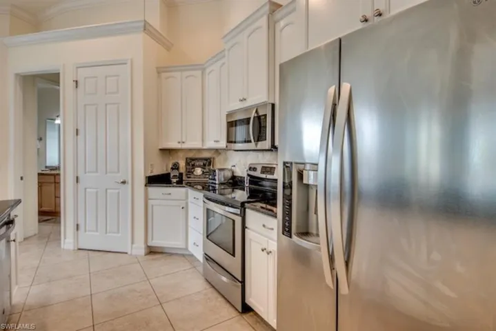Kitchen with backsplash, white cabinetry, ornamental molding, appliances with stainless steel finishes, and light tile floors