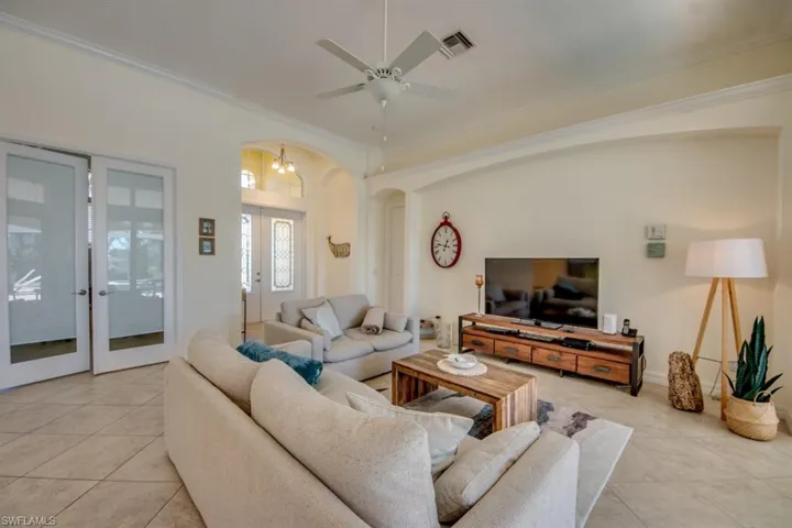 Living room featuring ceiling fan, crown molding, and light tile flooring
