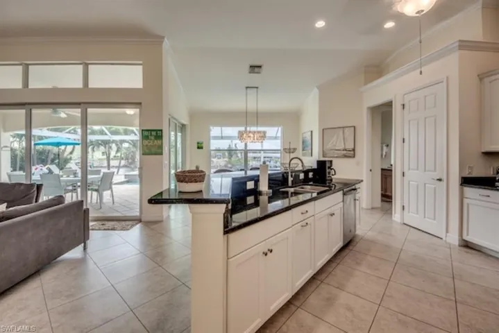Kitchen with a center island with sink, dishwasher, light tile flooring, and decorative light fixtures