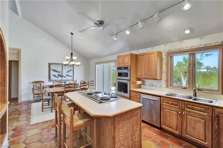 Kitchen featuring lofted ceiling, sink, hanging light fixtures, appliances with stainless steel finishes, and a kitchen island