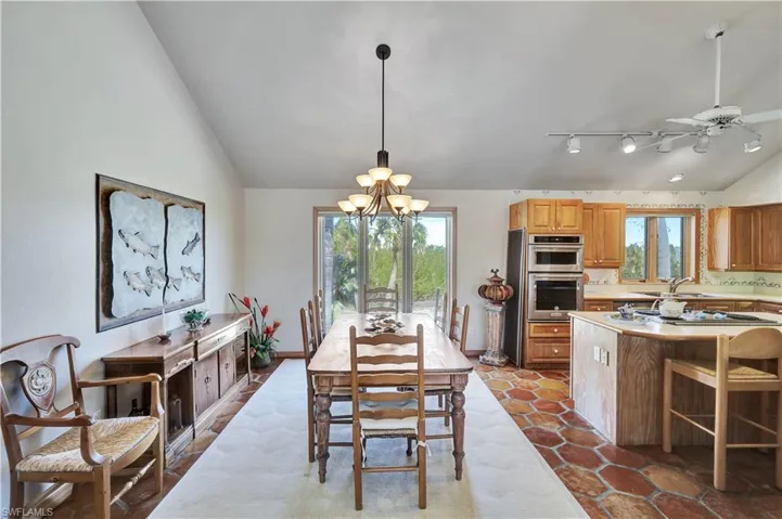 Dining room with vaulted ceiling, ceiling fan with notable chandelier, and light tile patterned floors