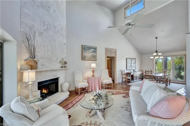Living room with a towering ceiling, a stone fireplace, and ceiling fan with notable chandelier