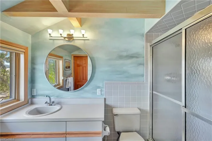 Bathroom with a shower with shower door, lofted ceiling, tile walls, vanity, and toilet
